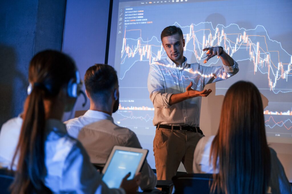 Male leader talking to employees, showing information on the projector in office